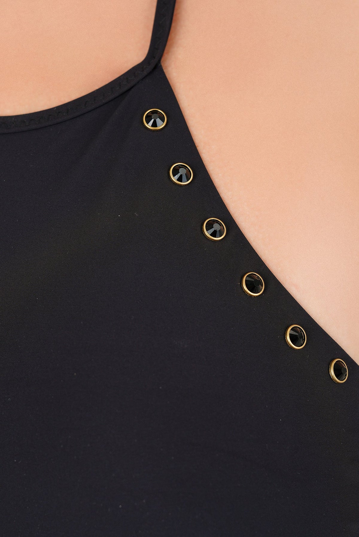 Detalle de ojillos dorados alineados sobre la tela negra del traje de baño completo